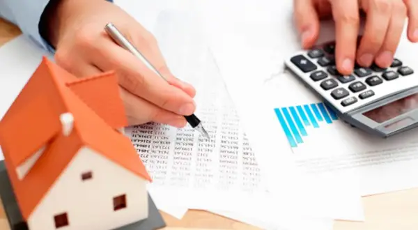 Man calculando el precio tasación vivienda con calculadora y modelo de casa.