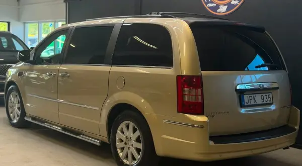 En gyllene Chrysler Voyager står parkerad. Den har en takbox och en svensk registreringsskylt.
