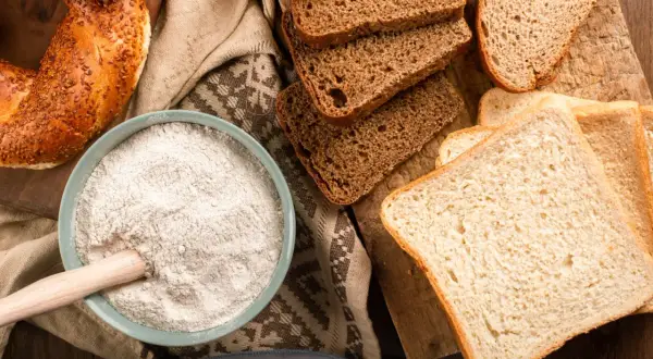 Mąka, chleb i bajgiel – oto główne źródła, w czym jest gluten. Składniki do wypieku na drewnianej desce.