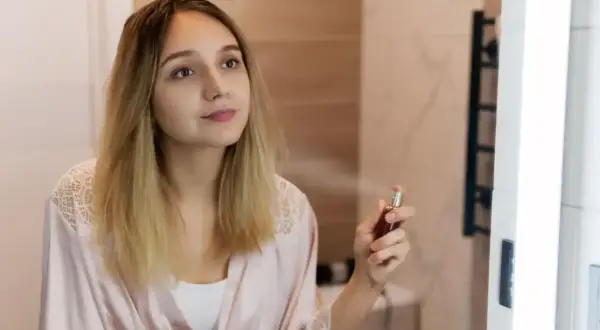 Młoda kobieta w szlafroku rozpyla perfumy. W powietrzu unosi się subtelny paczula zapach, otulając ją delikatną mgiełką.