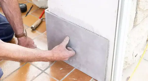 Pose d'un carrelage sur placo. Un artisan applique une plaque de carrelage gris sur un mur en placo, prêt à être collé.