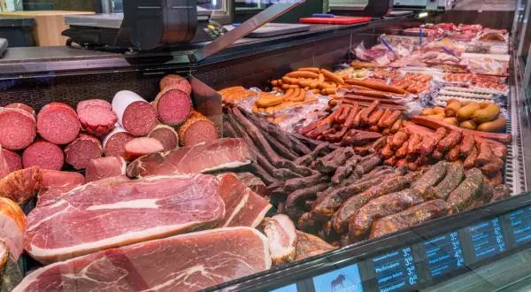 Reichhaltige Auswahl an bayerischer Wurst und Schinken, von Salami bis hin zu deftigen Rohwürsten, appetitlich präsentiert in einer Kühltheke.