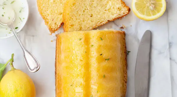 Un delizioso plumcake al limone glassato, con fette affettate, limoni freschi, una ciotolina di glassa e un coltello.