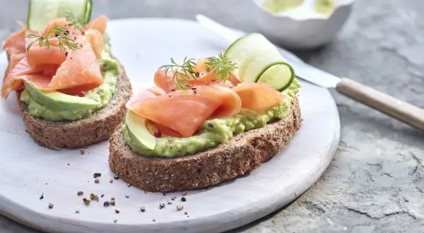 Deux toasts avocat saumon, garniture fraîche avec concombre et aneth, sur pain complet.