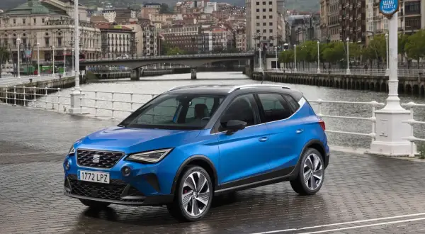 Blå Seat Arona parkerad vid en kaj med stad och broar i bakgrunden. Perfekt för en seat arona test i en europeisk stad.
