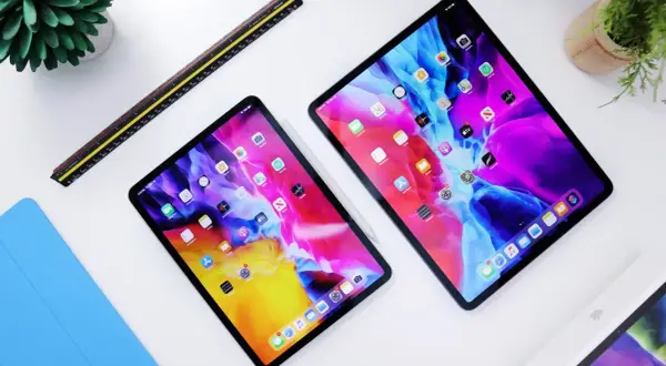 Dwa iPady z kolorową tapetą, obok linijka i niebieska okładka. Dowiedz się, jak przyspieszyć tablet.