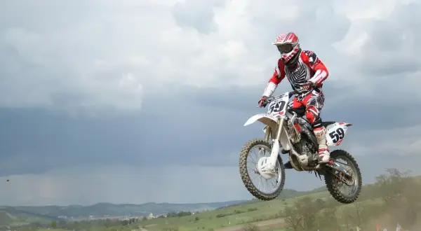Motocrossowiec w skoku na motocyklu, podobnym do Husqvarna Motorcycles i KTM, w czerwono-białym stroju.
