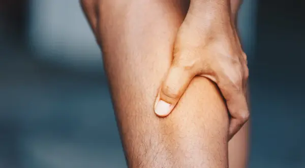 Hand greift an schmerzendes Bein. Was hilft gegen Muskelschmerzen?
