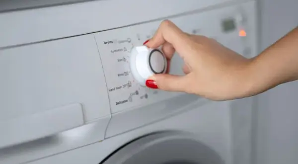 Main d'une femme sélectionnant le programme synthétique sur une machine à laver.