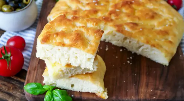Fluffiges Focaccia-Rezept: goldbraunes Brot mit knuspriger Kruste und weicher Krume, garniert mit frischem Basilikum und Tomaten.