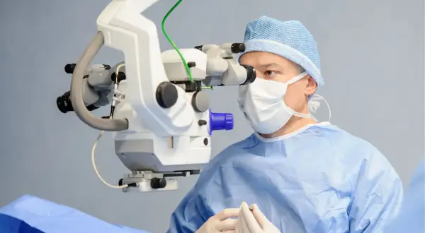 Chirurg w masce i czepku operacyjnym wykonuje trabekulektomię, używając mikroskopu.