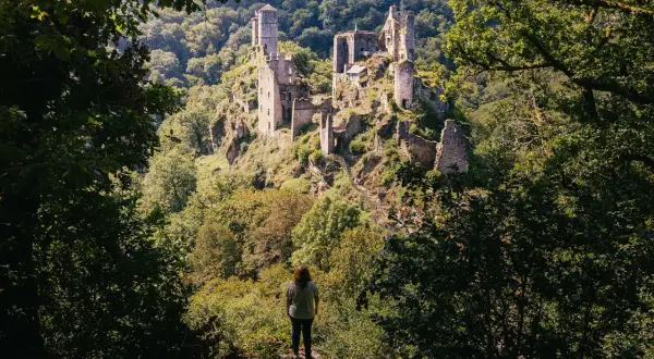 Une personne contemple les ruines d'un château perché sur une colline boisée. Une belle idée de que faire en Corrèze pour les amateurs d'histoire et de nature.