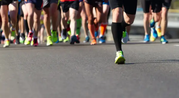 Gambe di corridori in maratona, con scarpe colorate. Un esempio di tabella maratona 4 allenamenti settimanali.