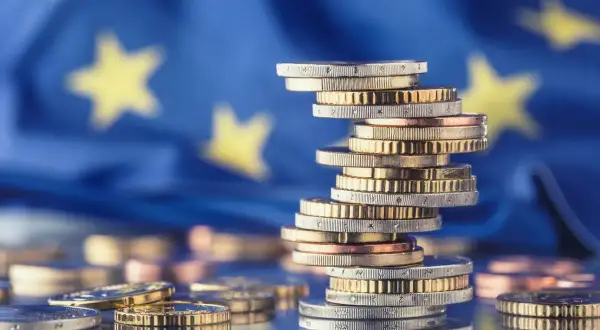 Stos monet euro na tle flagi UE symbolizuje pomoc de minimis dla przedsiębiorców.