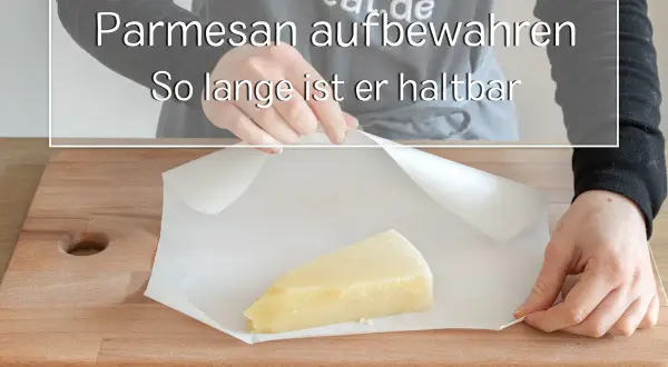 Ein Stück Parmesan wird auf Backpapier auf einem Holzbrett gelegt.
