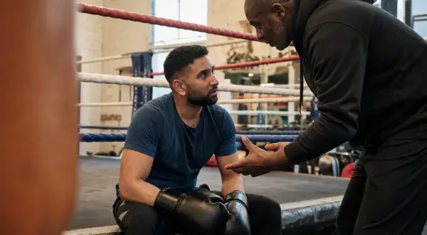A boxer, sweat on his brow, listens intently as his coach explains that boxing is hard, but worth it.