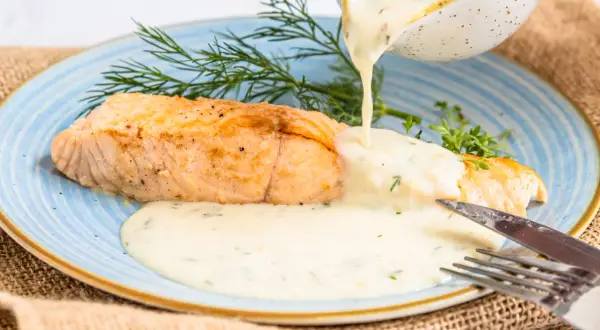 Ein goldbraunes Lachsfilet wird mit einer cremigen, Kräuter-haltigen Sauce übergossen. Perfekte Sauce zu gebratenem Lachs, garniert mit Dill.