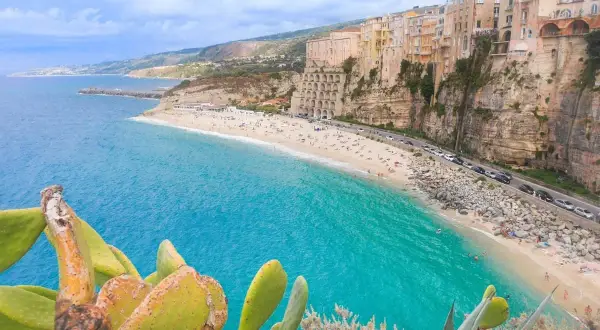 Vue panoramique de la plage de Tropea, Calabre, avec ses eaux turquoise, ses falaises et ses maisons colorées perchées.