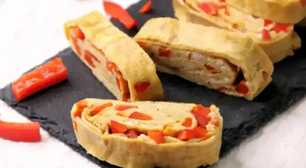 Roladki omlet tamago z papryką, ułożone na czarnej desce.