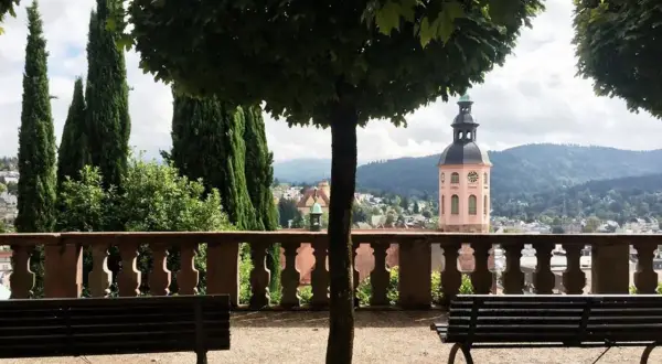 Ein friedlicher Tag in Baden-Baden: Bänke laden zum Verweilen ein, während im Hintergrund ein Kirchturm und grüne Hügel die Aussicht zieren.