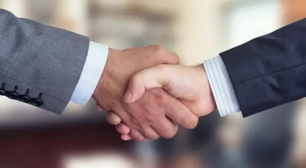 Dwaj mężczyźni w garniturach ściskają sobie dłonie, symbolizując udane joint venture i partnerstwo biznesowe.