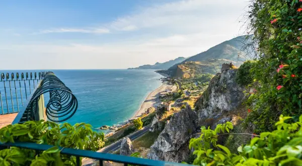 Balkonblick auf Siziliens Küste: Türkises Meer, felsige Hänge & blühende Pflanzen. Perfekt für Sizilien Urlaub Tipps!