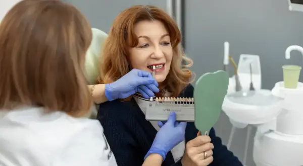 Dentystka pokazuje pacjentce wzornik kolorów, by dobrać idealny odcień licówek. Proces tworzenia pięknego uśmiechu.