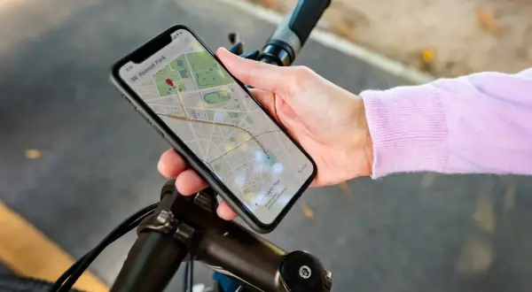 Dłoń trzyma smartfon z mapą, wskazującą trasę rowerową. Telefon pełni rolę licznika na rower, pokazując drogę do celu.