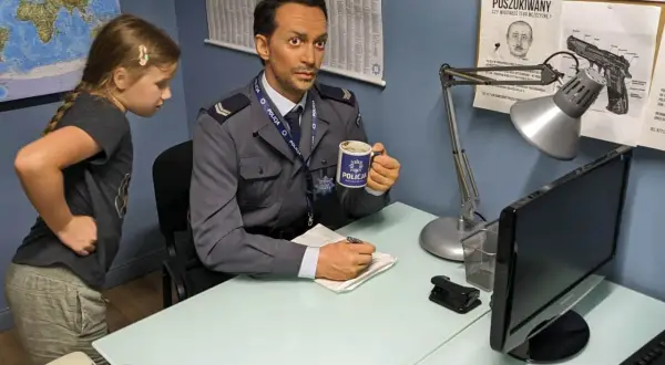 W muzeum Ojca Mateusza dziewczynka przygląda się woskowemu policjantowi z kubkiem "POLICJA".
