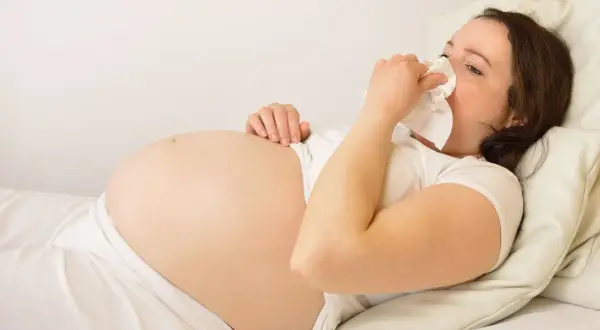 Gravid kvinna med andfåddhet ligger i sängen och snyter sig i en näsduk.
