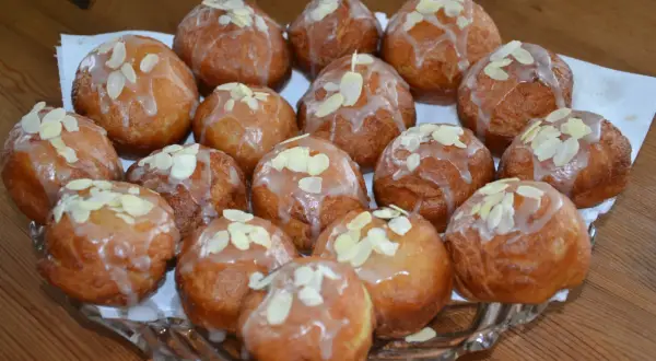 Pyszne pączki z adwokatem, polane lukrem i posypane płatkami migdałów, ułożone na szklanej paterze.