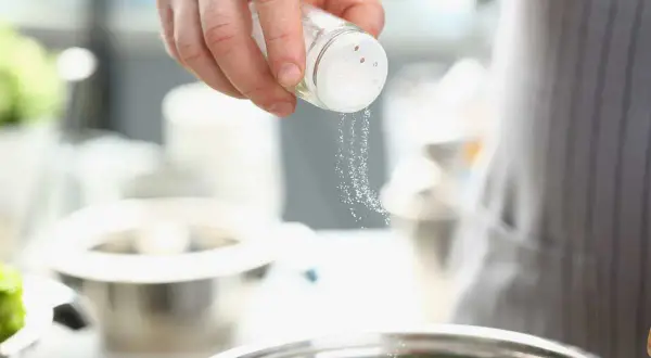 Une main saupoudre du sel dans un bol, ajoutant une touche de saveur à la cuisine.