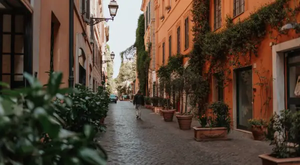 Eine Person geht durch eine schmale Gasse in Rom, gesäumt von orangefarbenen Gebäuden und Pflanzen. Ein perfekter Ort für Rom Geheimtipps.