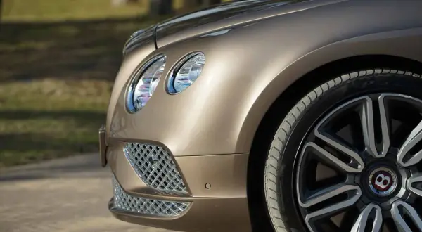 Detaljbild av en lyxig, brun Bentley till salu. Framhjulet och strålkastaren syns tydligt.