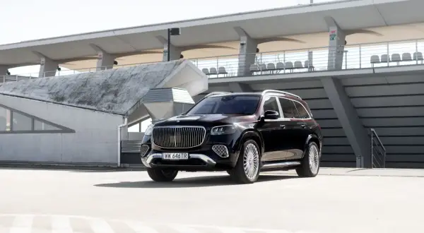 Elegancki, czarny Mercedes GLS Maybach z chromowanymi detalami i charakterystycznym grillem, zaparkowany na tle nowoczesnej architektury stadionu.