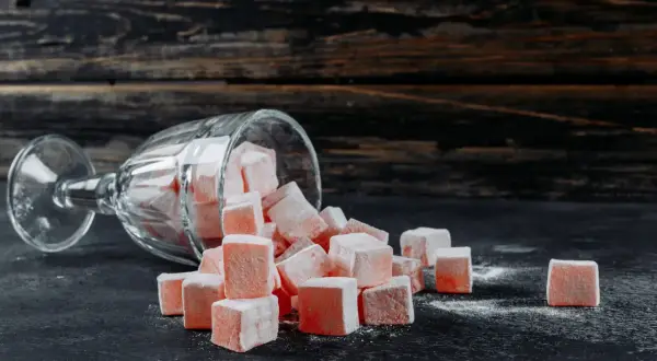 Un verre renversé d'où tombent des cubes de loukoum roses saupoudrés de sucre glace.