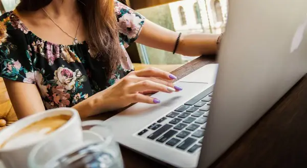Ragazza con laptop e caffè, mentre cerca la differenza ferie e permessi.