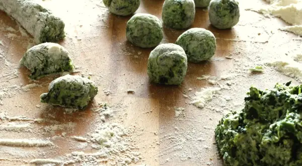 Zielone, domowe gnocchi ze szpinakiem, obtoczone mąką, czekają na ugotowanie.
