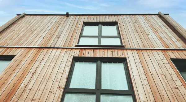 Moderne Holzfassaden Beispiele: Natürliche Holzverkleidung mit großen Fenstern unter blauem Himmel.