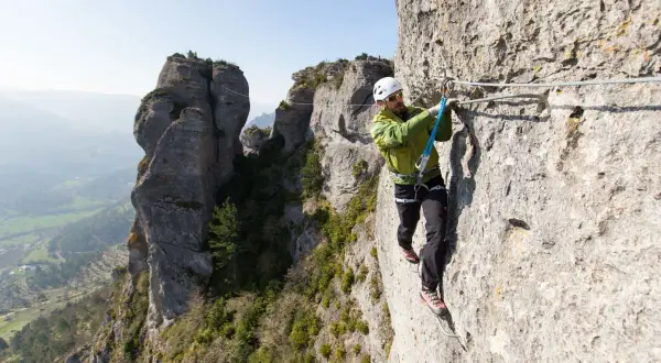 Un homme équipé pour la via ferrata progresse sur une paroi rocheuse, profitant d'un paysage spectaculaire.