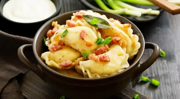 Pyszne pierogi z boczkiem i szczypiorkiem. Wiesz, ile gotować pierogi, by były idealne? Podane z kwaśną śmietaną.