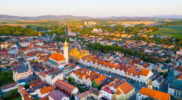 Luftaufnahme eines malerischen **Taus Tschechien** mit roten Dächern, einer Kirche und grünen Hügeln im Hintergrund.