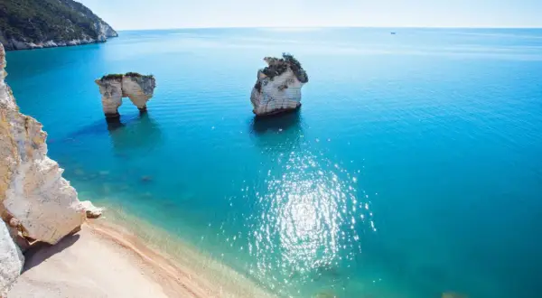 Faraglioni iconici sulla costa del Gargano, bagnati da un mare cristallino e soleggiato.
