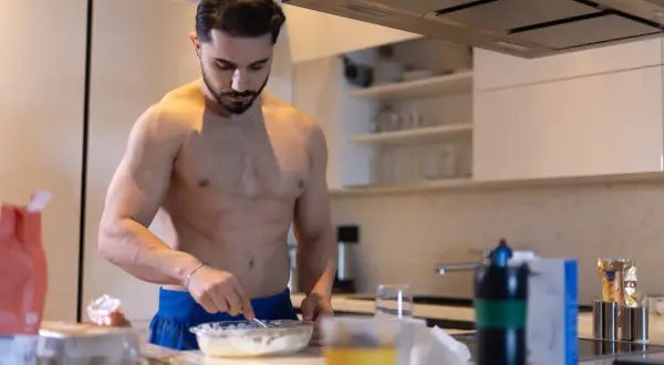 Muskulöser Mann bereitet in der Küche eine Mahlzeit zu. Kohlenhydrate sind wichtig für den Muskelaufbau.