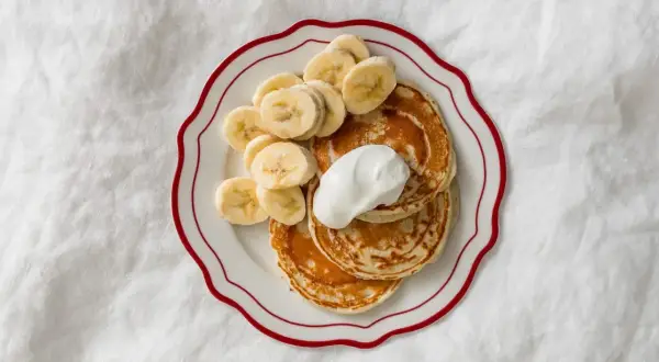 Pyszne placuszki bananowe dla dzieci, udekorowane plasterkami banana i kleksem śmietany. Idealne na śniadanie!