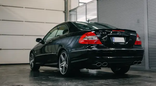 Czarny Mercedes CLK 63 AMG z podwójnymi końcówkami wydechu, zaparkowany w garażu z podnoszoną bramą.