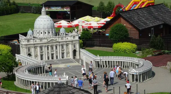 Miniaturowy park z modelem Bazyliki św. Piotra i placem Berniniego. W tle zjeżdżalnia i budynki. Sprawdź inwałd park cennik.