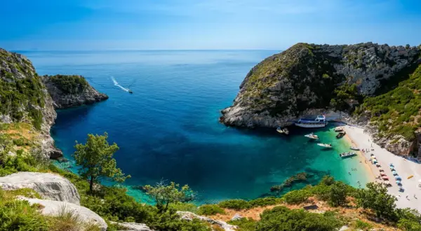 Malownicza zatoka z krystalicznie czystą wodą i plażą, gdzie cumują łodzie. Idealne miejsce na wakacje, zastanawiasz się, ile się leci do Albanii?
