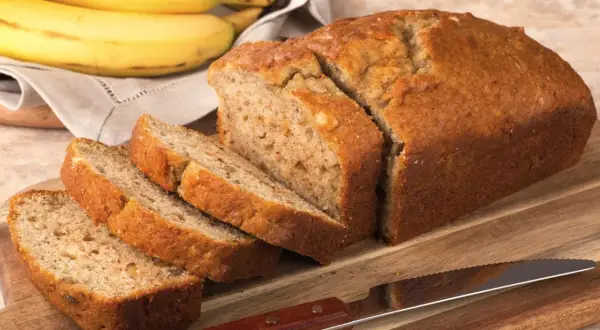Pokrojony, złocisty chlebek bananowy, obok pęk dojrzałych bananów. Idealny na najprostszy chlebek bananowy.