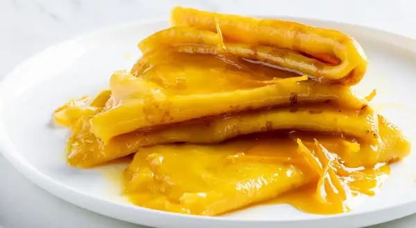 Pila di crepes suzette dorate, ricoperte da una salsa all'arancia lucida e invitante.